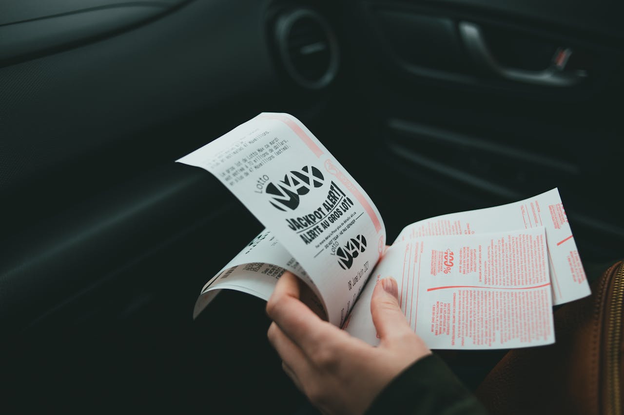 about-us Close-up of hands holding Lotto Max papers inside a car, symbolizing luck and chance.