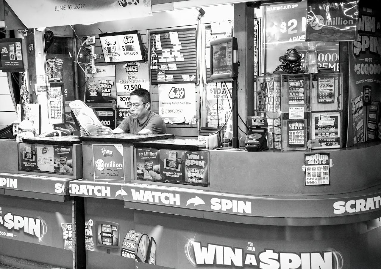 discover A man reads at a busy lottery ticket booth filled with signs and advertisements.